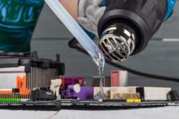 Close up of an industrial hair dryer melting a polymer stick onto a PCB.