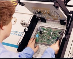 A RiverSide employee in the early 90s places a completed circuit board onto a pins tester, which was then brand new technology.